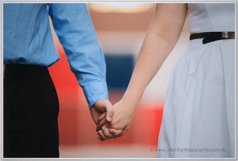 Close crop of Julie and Dale clasping hands, red and blue panels blurred behind