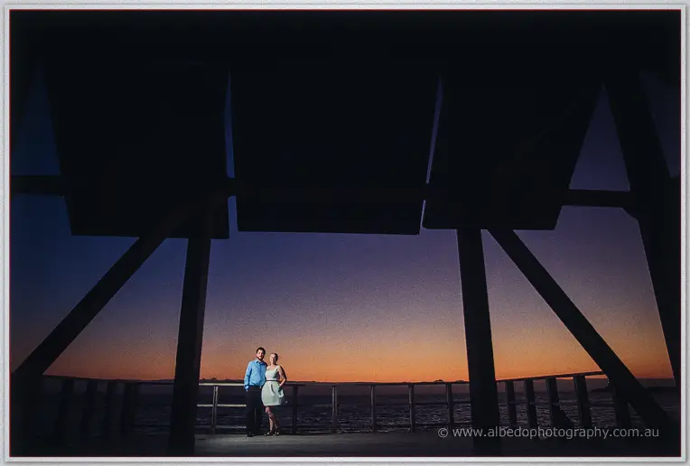 Beneath the jetty's shadowed timbers, Julie and Dale are lit against a violet twilight sea