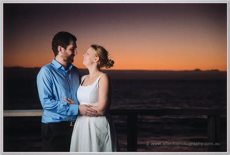 Julie embraces Dale from behind as they gaze at each other in the dusk afterglow