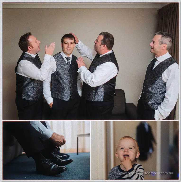 Groomsmen in paisley vests ruffle Max's hair while his toddler chews a finger below their polished shoes.
