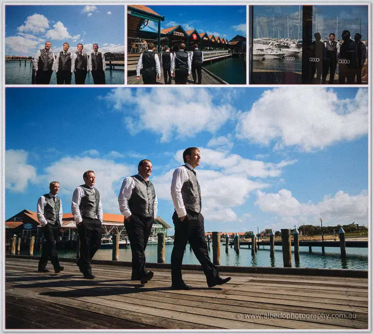 Max leads groomsmen along the sunlit Hillarys boardwalk, moored boats and blue water behind them.