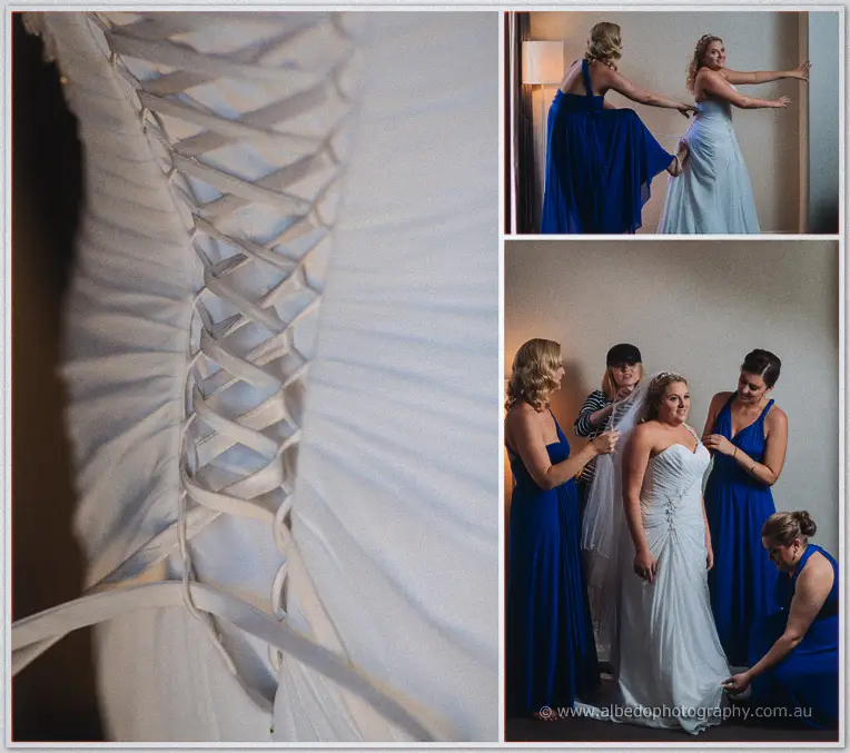 Corset lacing detail beside bridesmaids in blue easing Olivia into her gown and arranging her veil.