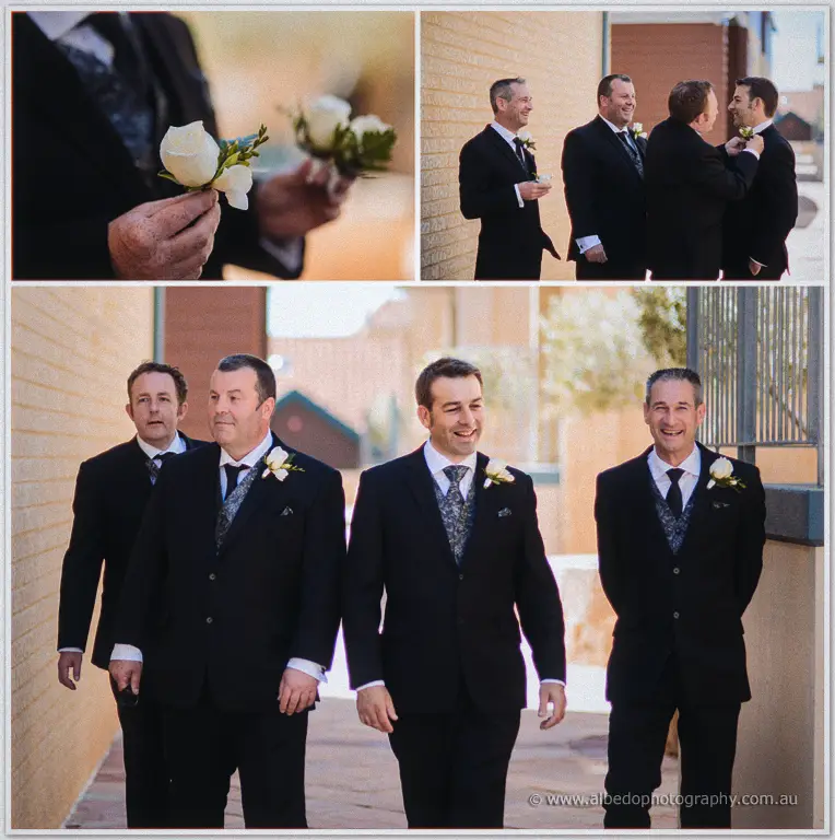 Groomsmen pin white rose boutonnieres and laugh together outside the brick Breakwater buildings.