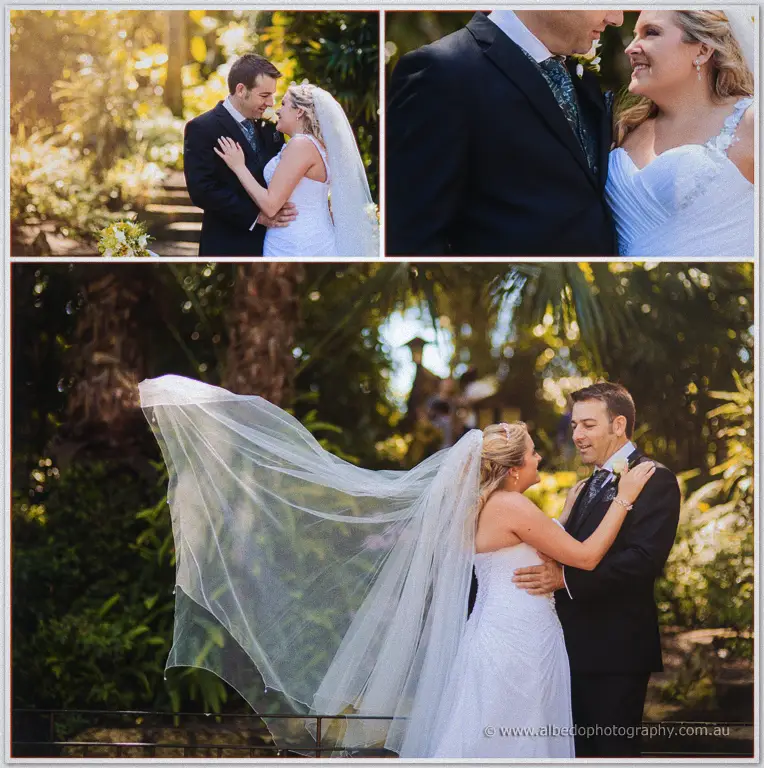 Olivia hugs Max from behind on a garden stairway, framed by palms and a stone bridge far above.