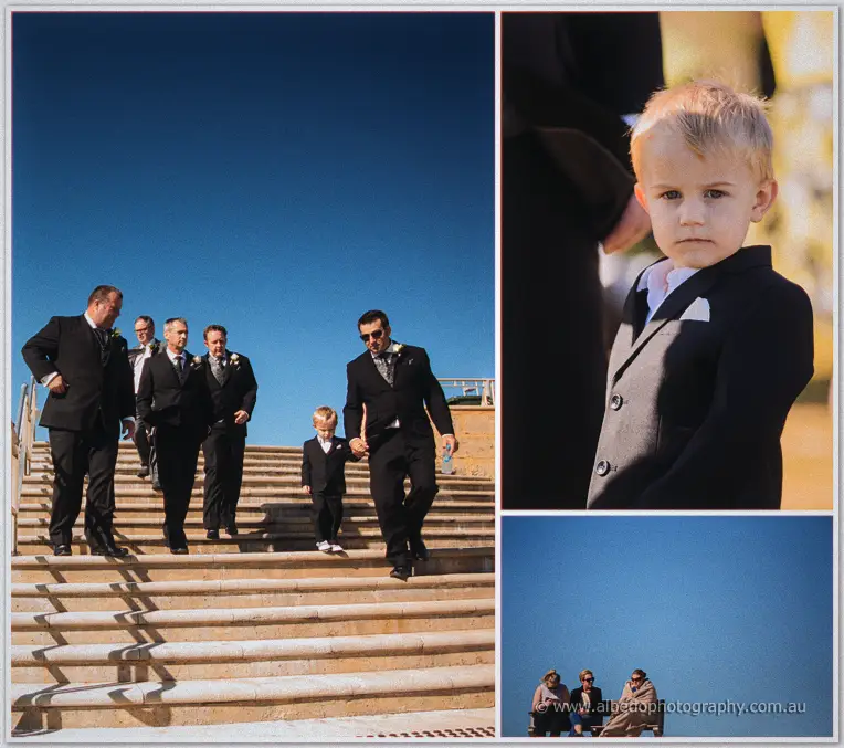Max leads groomsmen down sunlit stone steps with his small son as a page boy in a dark suit.