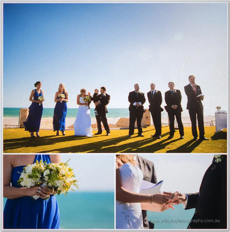 Olivia and Max marry on a lawn by the sea, bridesmaids in blue beside them before rings are placed.