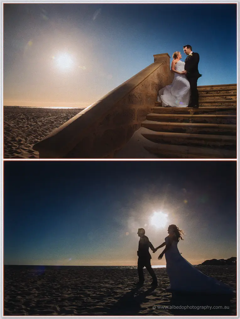 Olivia and Max stand close on stone beach steps as the setting sun flares over the sand dunes.