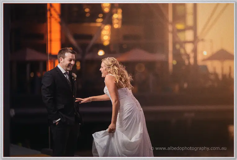 Olivia reaches playfully for laughing Max on the Hillarys marina boardwalk amid golden dusk light.