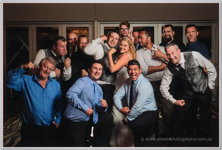 Olivia flexes with a big group of laughing guests in a playful pose at the reception.