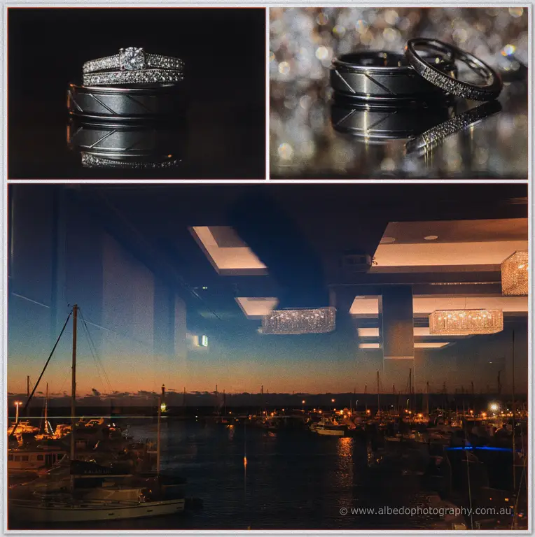 Olivia and Max's diamond rings gleam on dark glass above the sparkling twilight marina reflection.