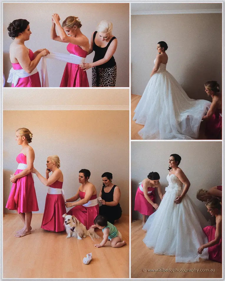 Bridesmaids in pink help Sarah into her gown as her dog and a toddler wander the bedroom floor.
