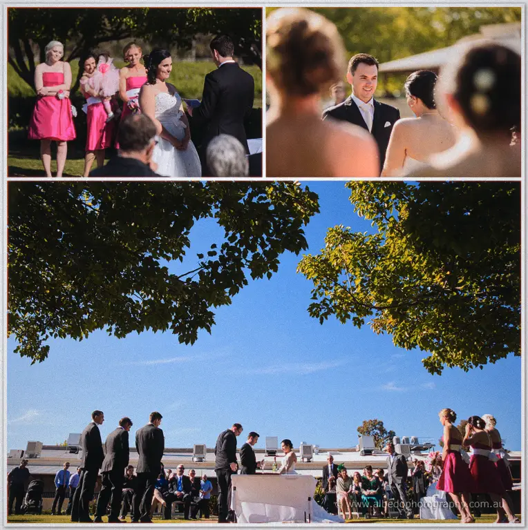 Bridesmaids watch the vows from the shade, wide frame showing the celebrant table and gathered guests.
