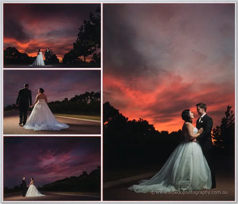 Sarah and Chris stand close on the road under a vivid pink and red sunset blazing over the vineyard.