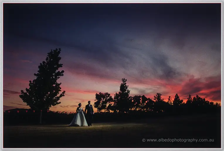 Sarah and Chris stand together in a field beneath a huge purple and orange twilight sky.