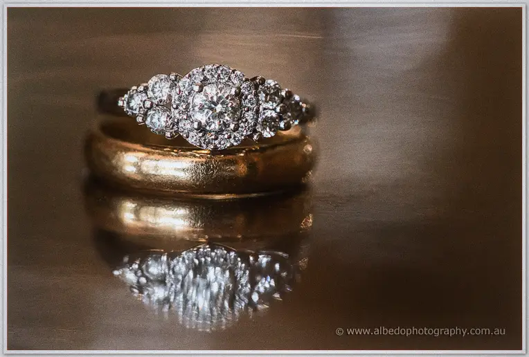 Tara's diamond halo engagement ring and gold wedding band rest on a polished table in warm window light
