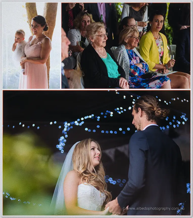 Tara and Stephen hold hands beneath strings of blue fairy lights as guests watch from their garden chairs