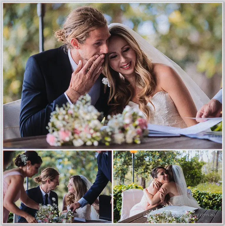 Stephen cups Tara's cheek as they sign the register beside pastel bouquets in the garden