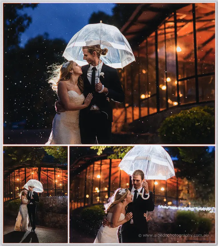 Tara and Stephen shelter under a clear umbrella in the rain among fairy-lit trees at Darlington Estate