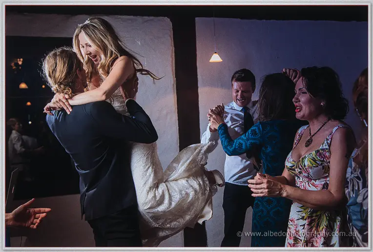 Stephen swings Tara off her feet as dancing guests fill the lamplit stone barn