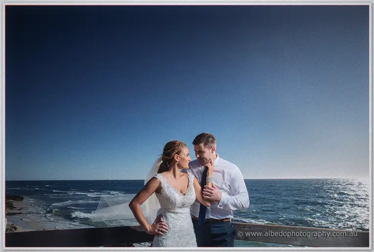 Tarmecca rests a hand on Lee's chest as sunlight glitters across the ocean behind them