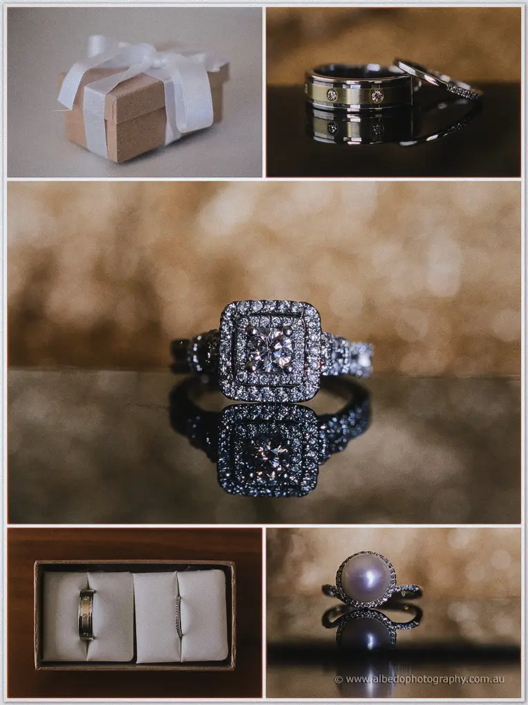 Wedding rings, a diamond engagement ring and pearl ring photographed beside a ribboned gift box