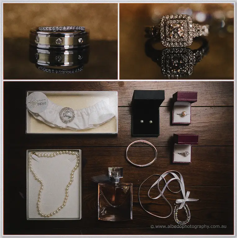 Flat lay of Prue's bridal accessories with pearl necklace, garter, perfume and rings on dark timber