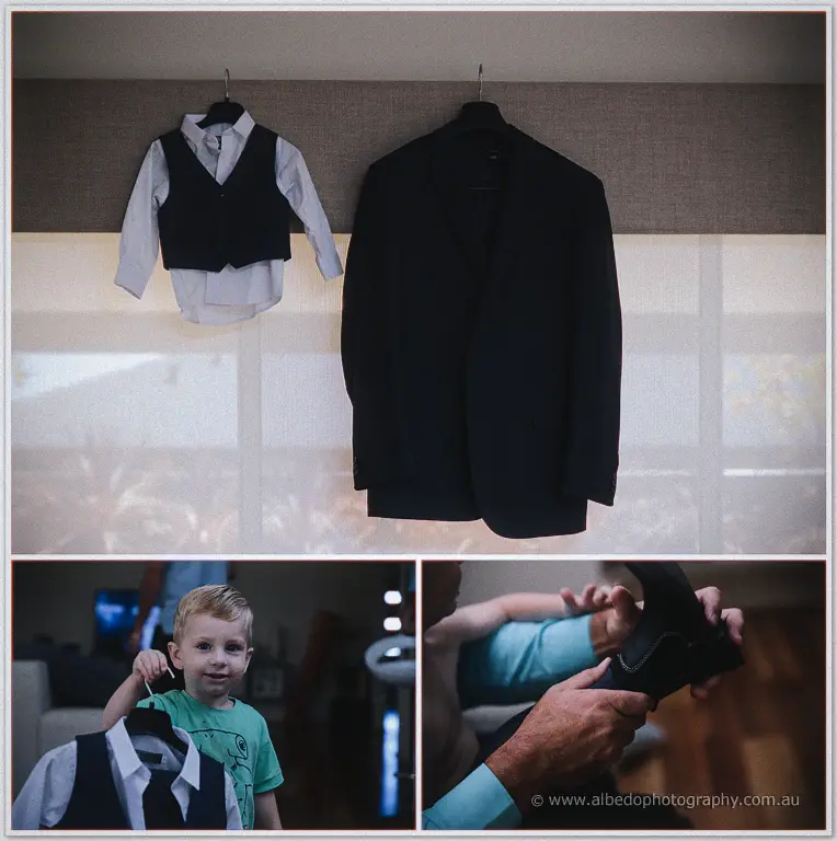 Groom's suit and page boy's vest hanging by a bright window as wedding preparations get under way