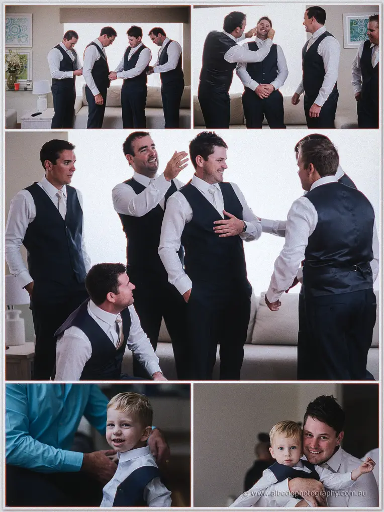 Groomsmen in navy vests joking together on the couch as they help each other dress