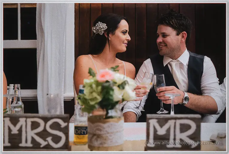 Prue and Michael toasting glasses at the bridal table behind MR and MRS blocks
