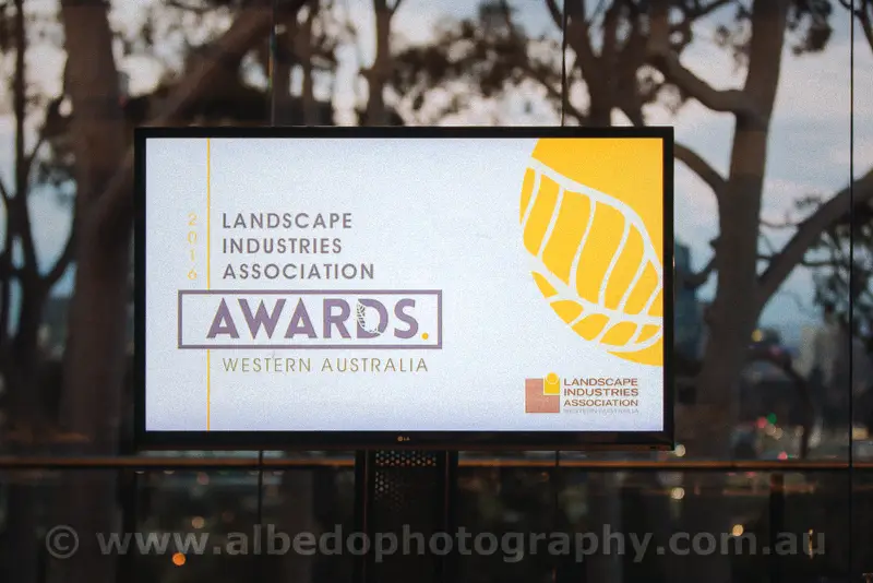 Screen glowing with the landscape awards emblem against rain-speckled glass at dusk