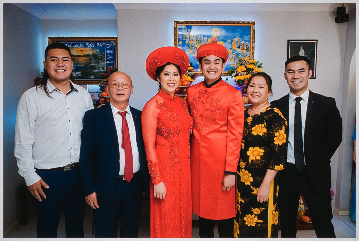 Natalie and Andrew in red traditional dress pose with their family in front of the family altar