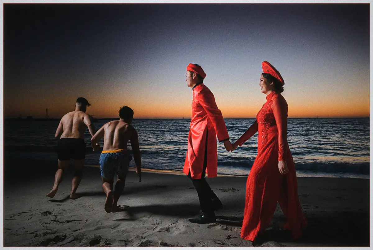 Natalie and Andrew hold hands on the twilight beach as friends run laughing to the water