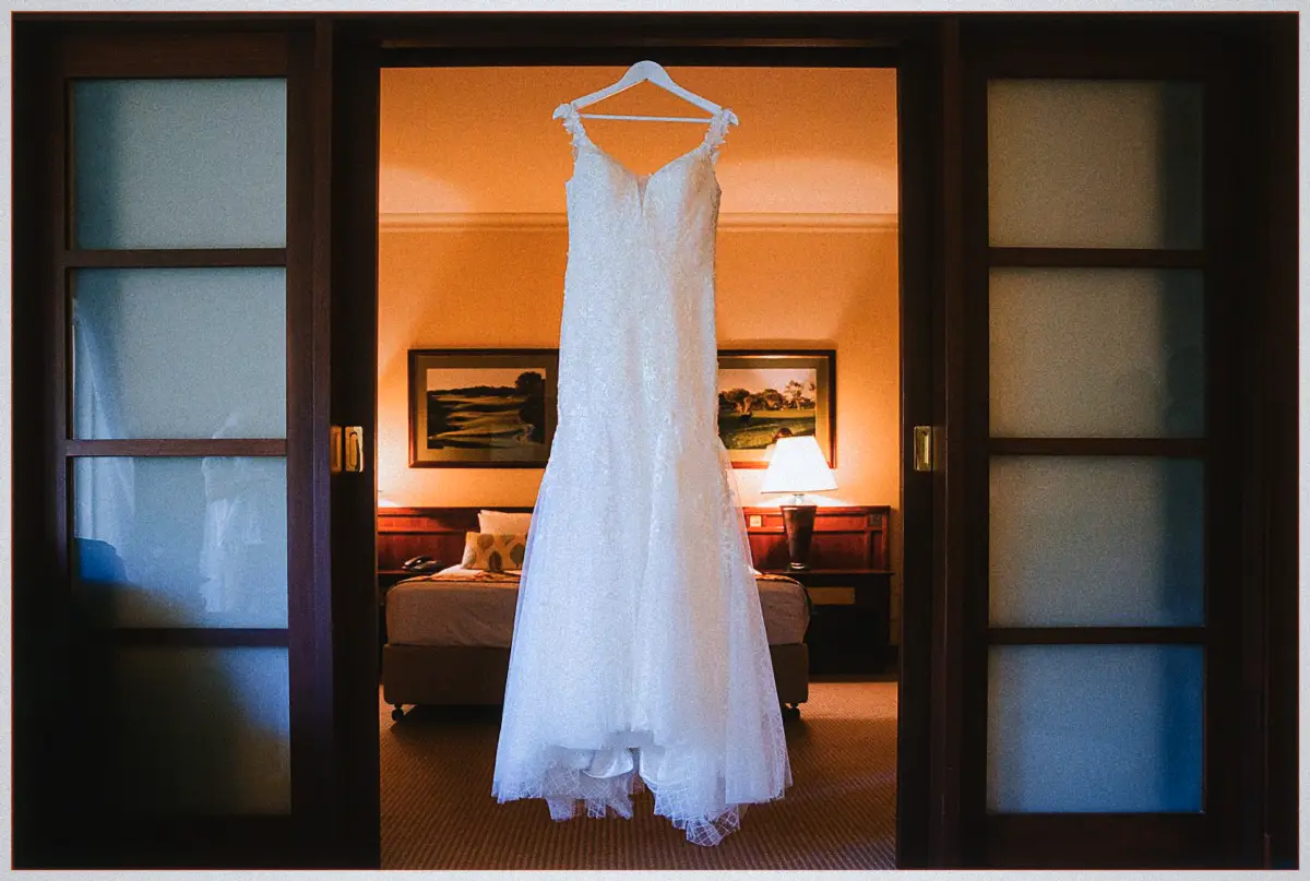 Natalie's lace wedding gown hangs in a doorway of the softly lit hotel suite