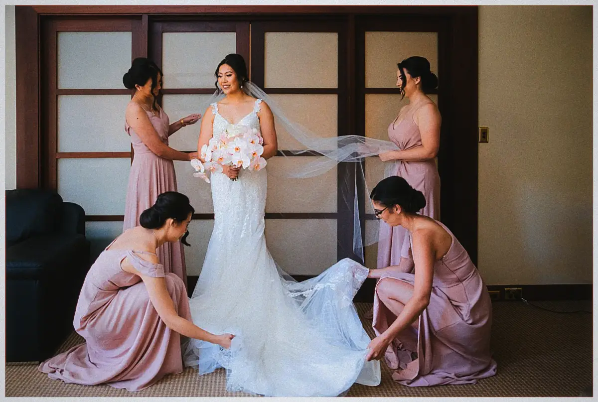 Bridesmaids in dusty pink arrange Natalie's veil and train as she holds an orchid bouquet