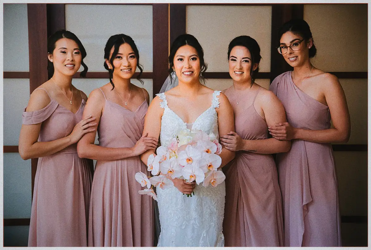 Natalie and her four bridesmaids in mauve dresses smile together holding the orchid bouquet