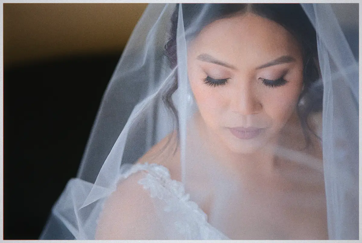 Natalie gazes down beneath her veil, lashes highlighted, in a soft bridal close-up