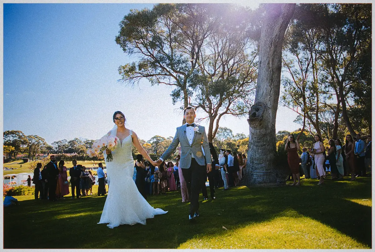 Natalie and Andrew stroll hand in hand down the lawn aisle past smiling guests in golden afternoon light