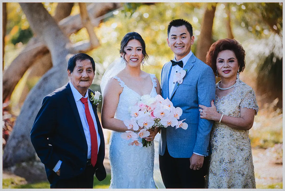 Natalie and Andrew pose smiling between two older relatives beneath golden-lit trees at Joondalup Resort