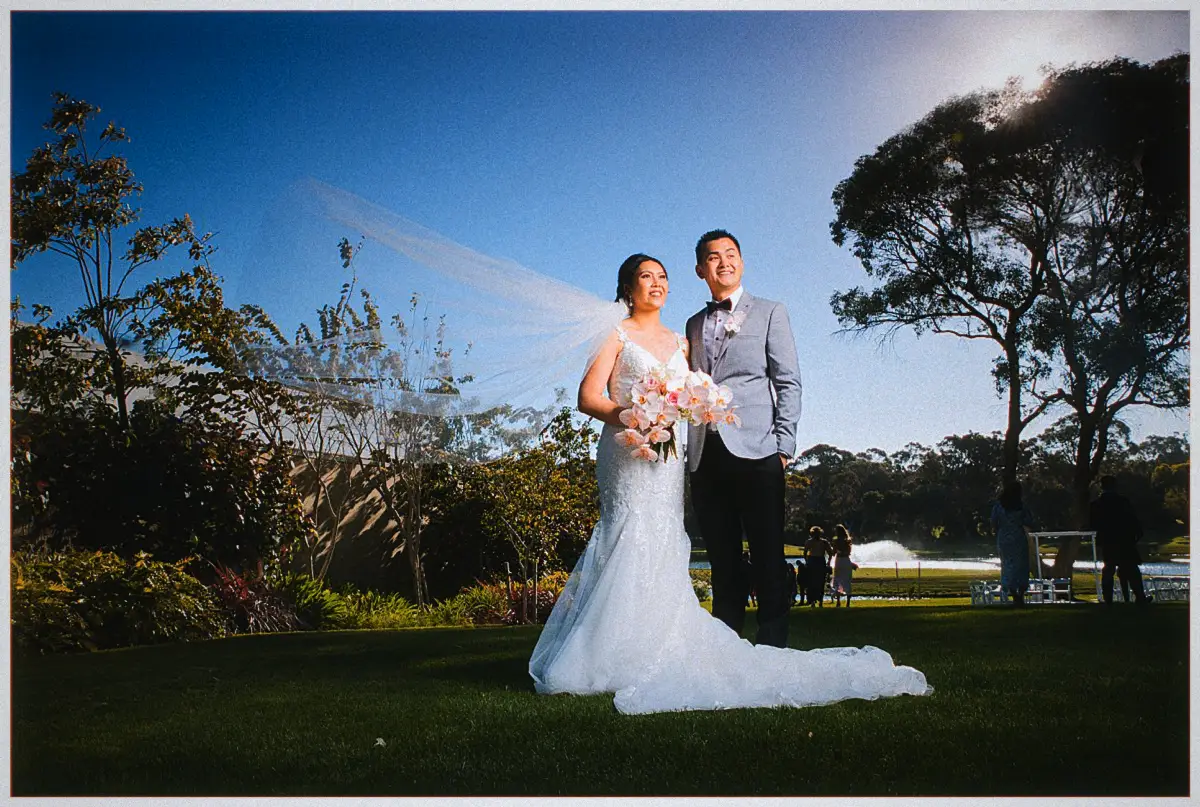 Natalie's veil billows as she and Andrew pose on the lawn beneath a deep blue Joondalup Resort sky