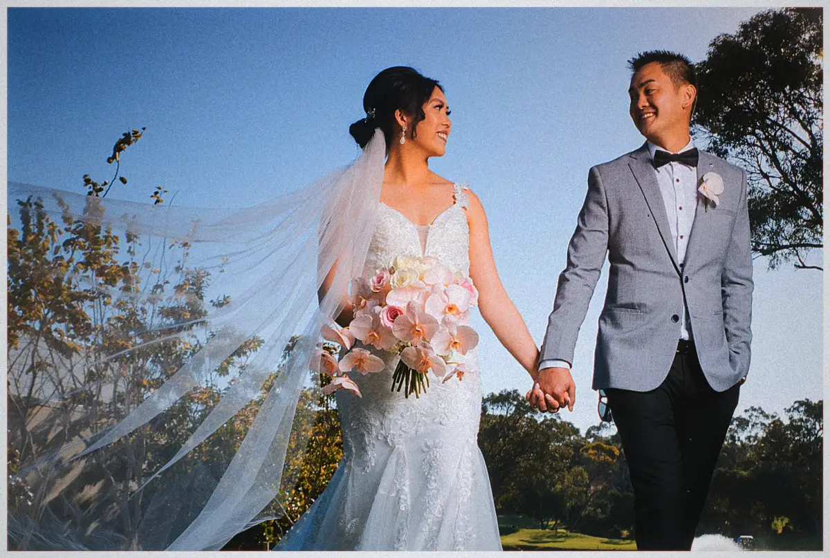 Natalie and Andrew walk hand in hand at golden hour, her long veil streaming behind them