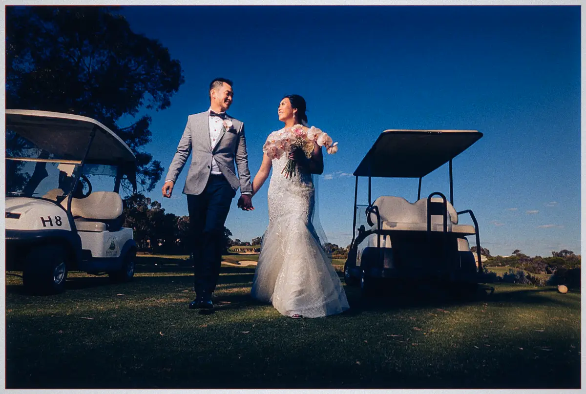 Natalie and Andrew stroll between parked golf buggies on the course under a deep blue evening sky