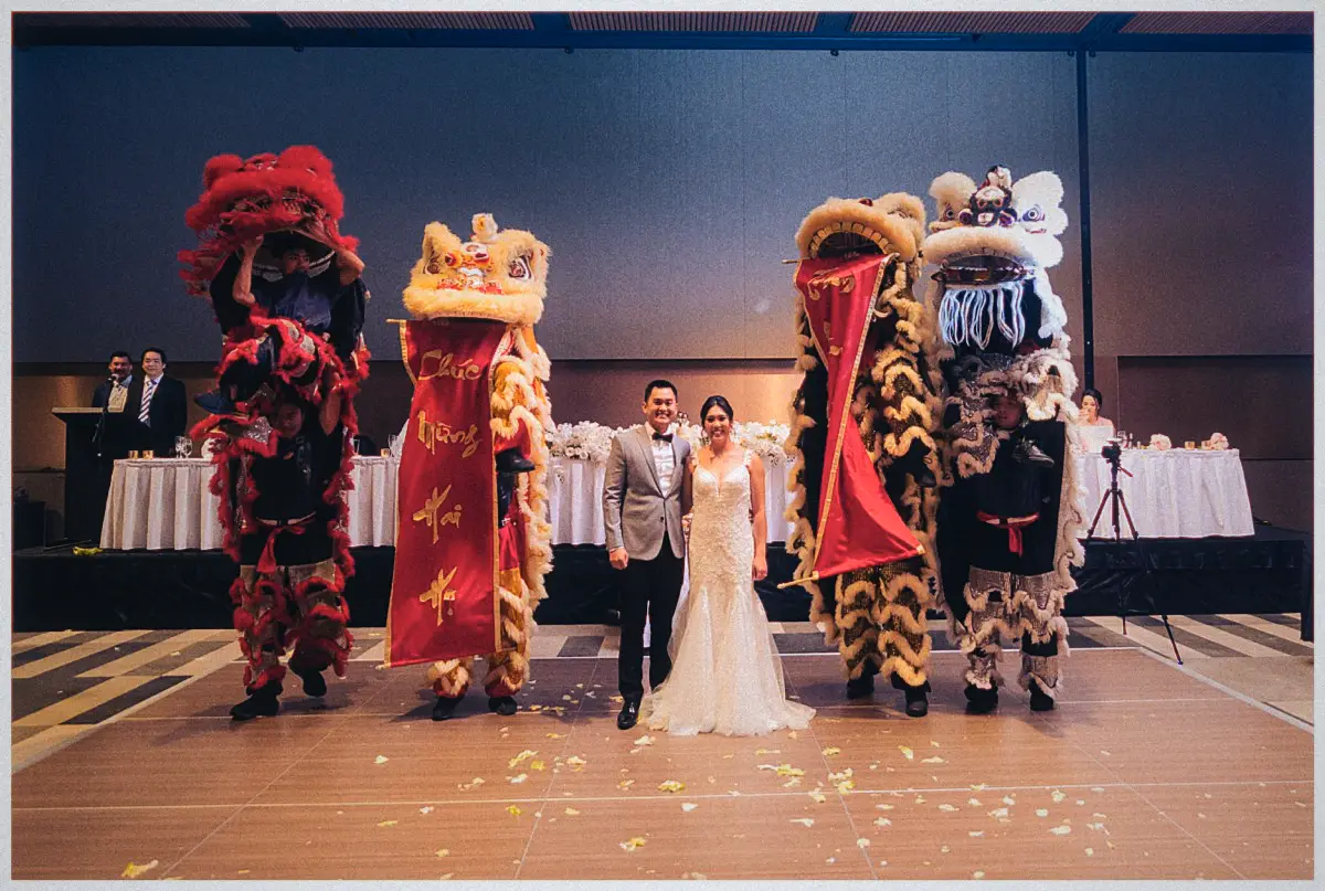 Natalie and Andrew flank four lion dancers waving red good-luck banners across the confetti-strewn dance floor