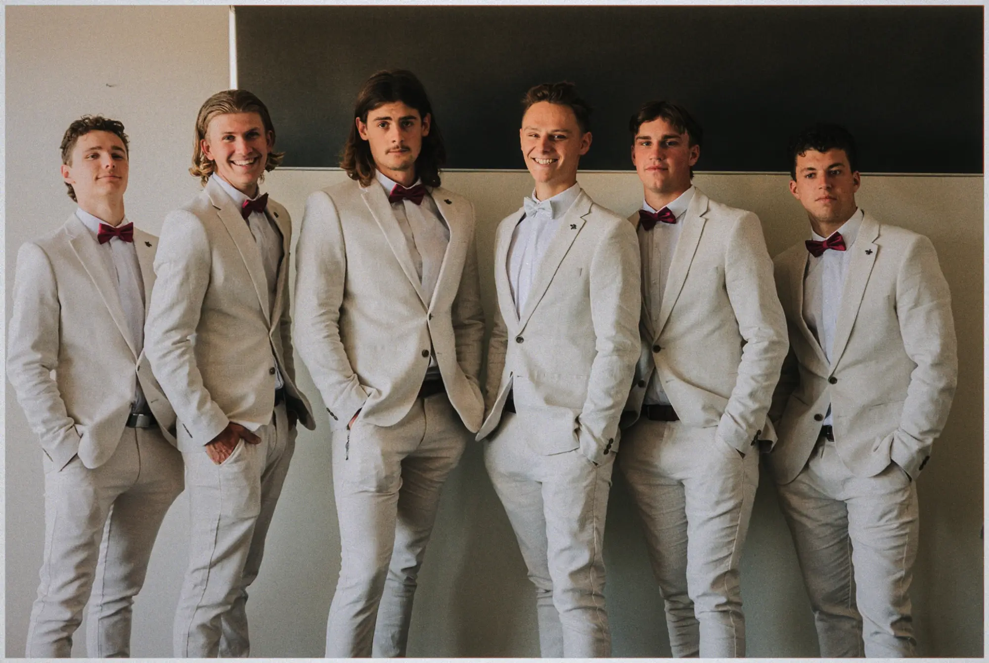 Justin and his five groomsmen line up in cream suits and burgundy bow ties, hands in pockets.
