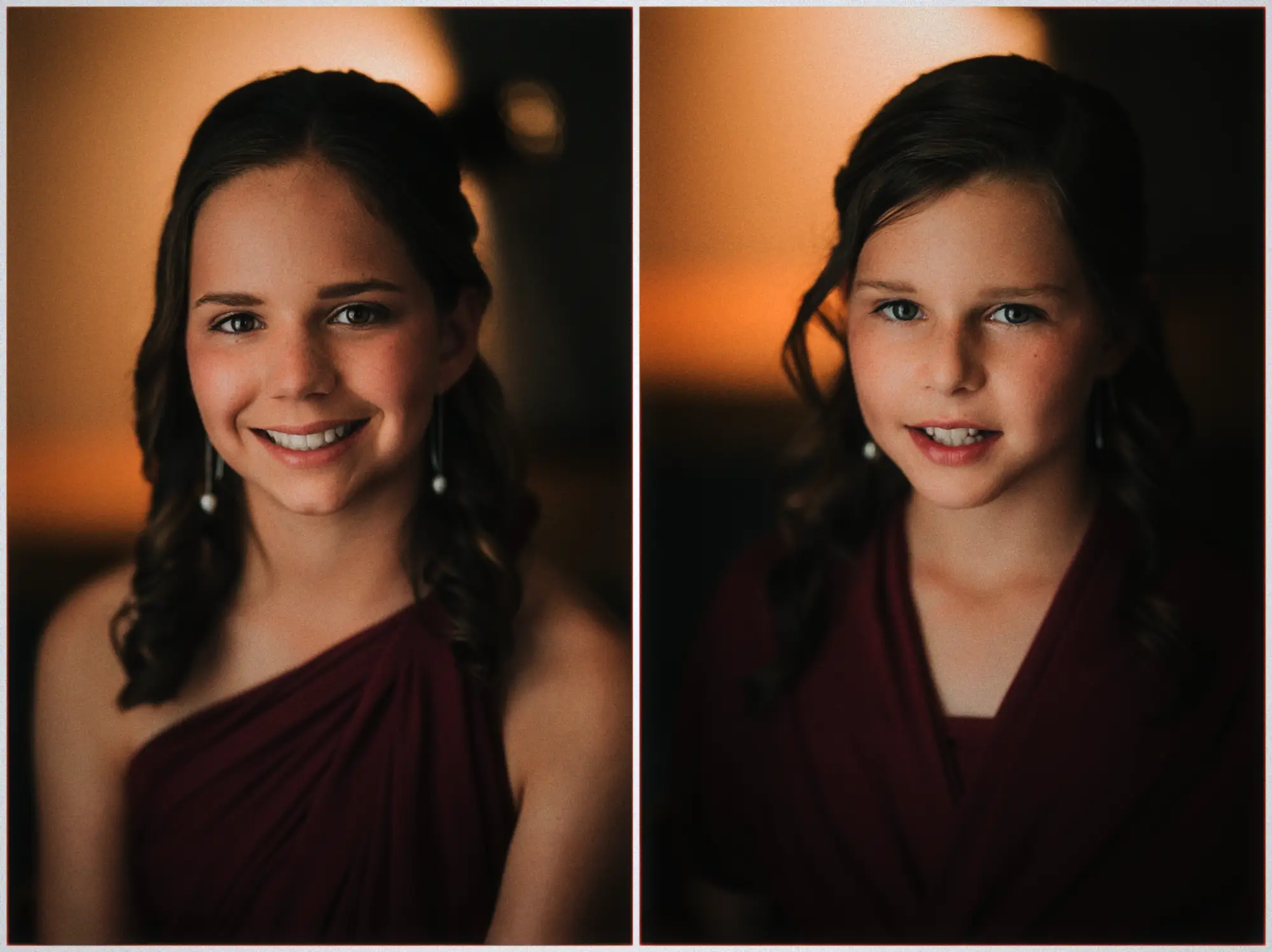 Two junior bridesmaids in burgundy one-shoulder dresses beam against amber lamp glow.
