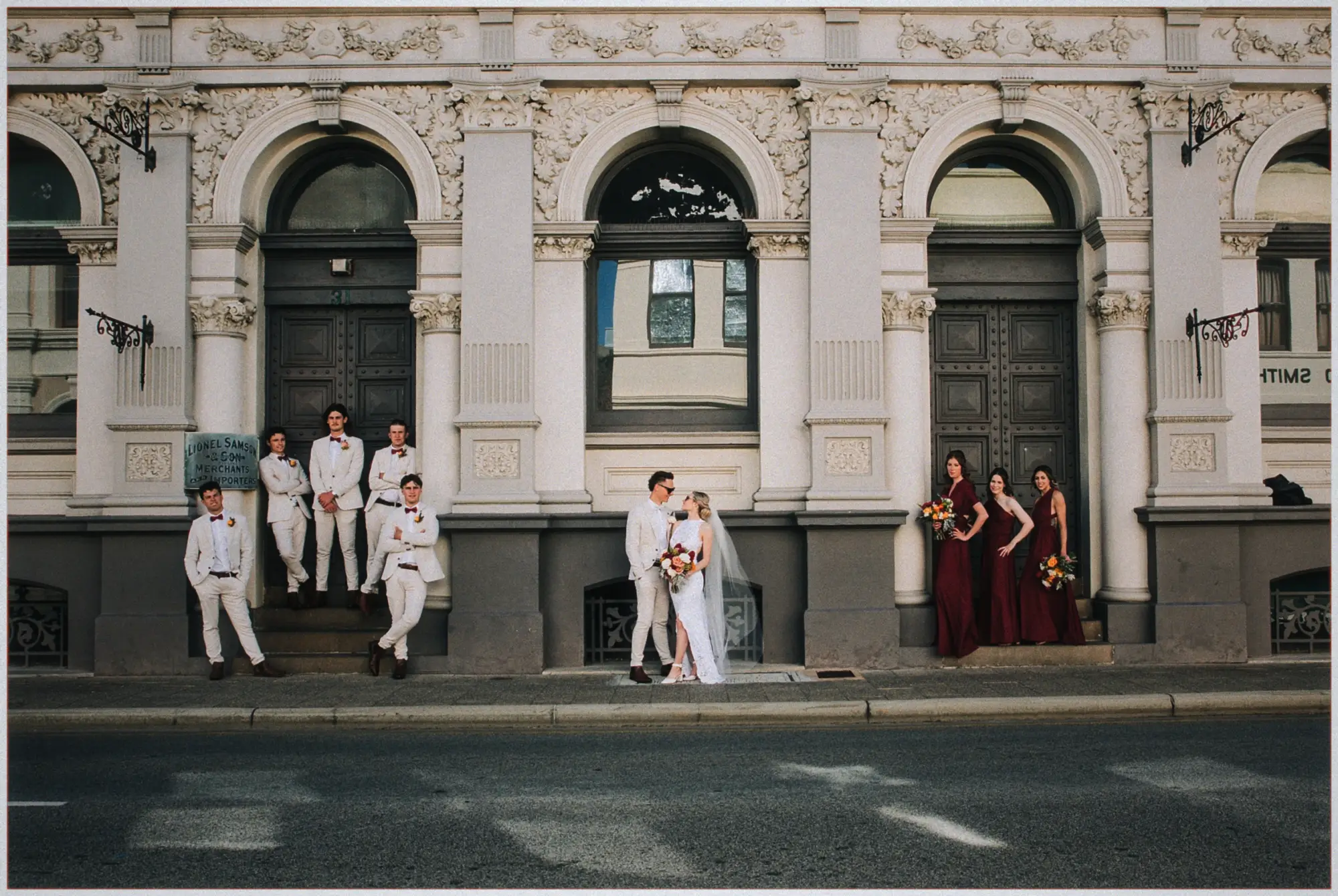 Groomsmen on heritage doorsteps, bridesmaids by a second door, Erin and Justin kissing between them.
