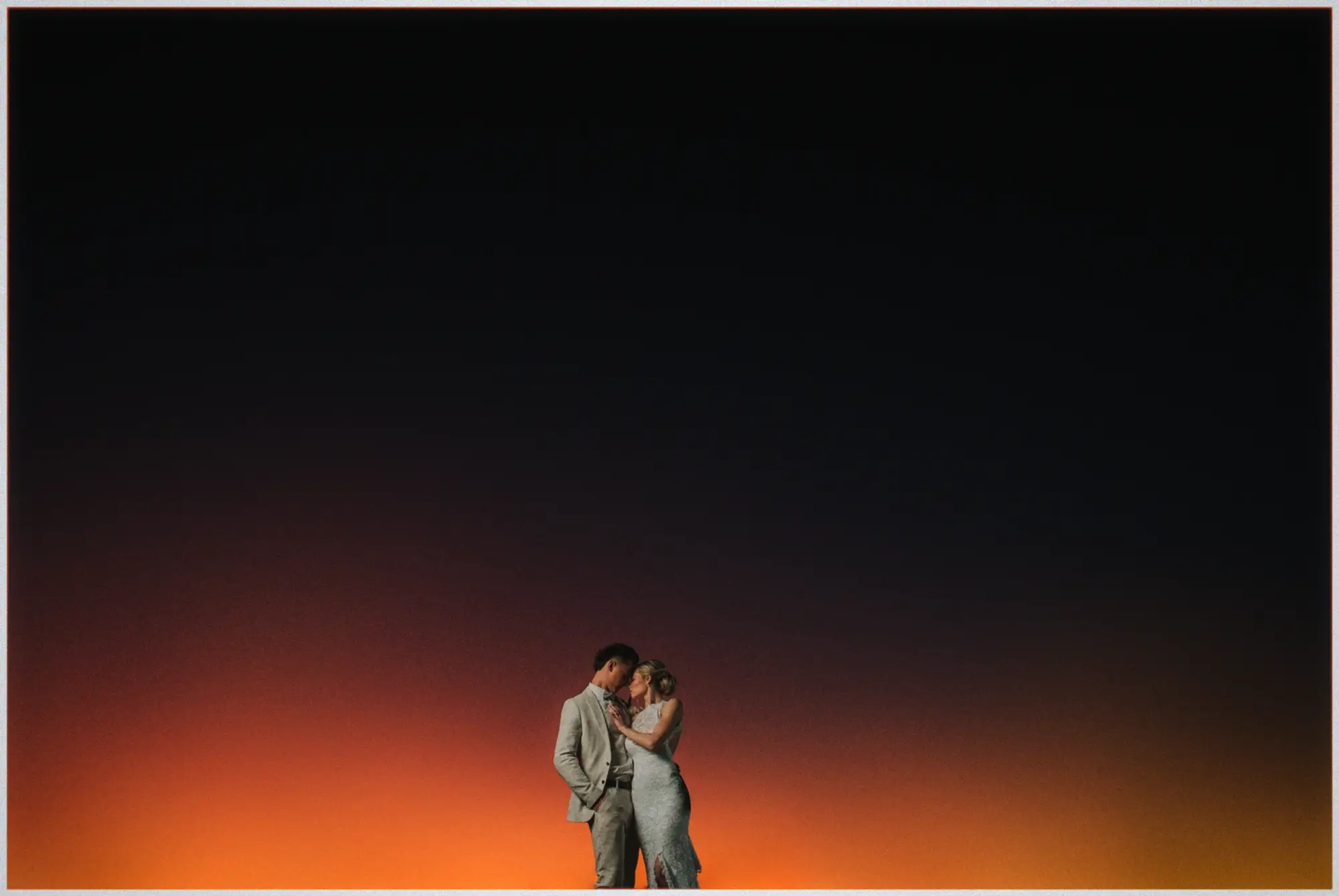 Erin and Justin kiss against a glowing orange dusk sky fading into darkness over Fremantle.